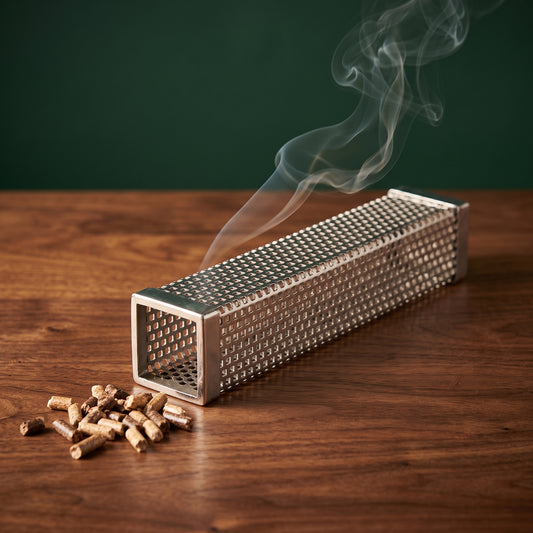 Smokestack pellet smoker tube with pellets and drifting smoke on a walnut table, Big Ron BBQ catalog