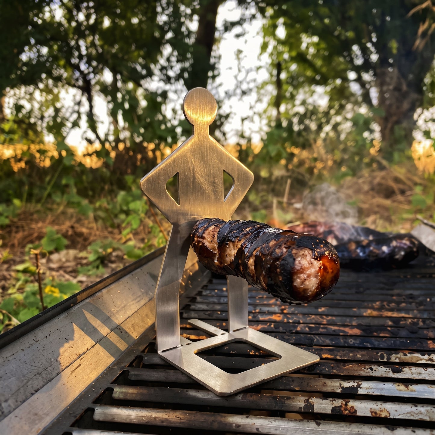 Big Ron stainless steel sausage holder standing on a grill holding a bratwurst