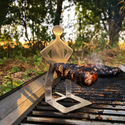 Big Ron stainless steel sausage holder standing on a grill holding a bratwurst